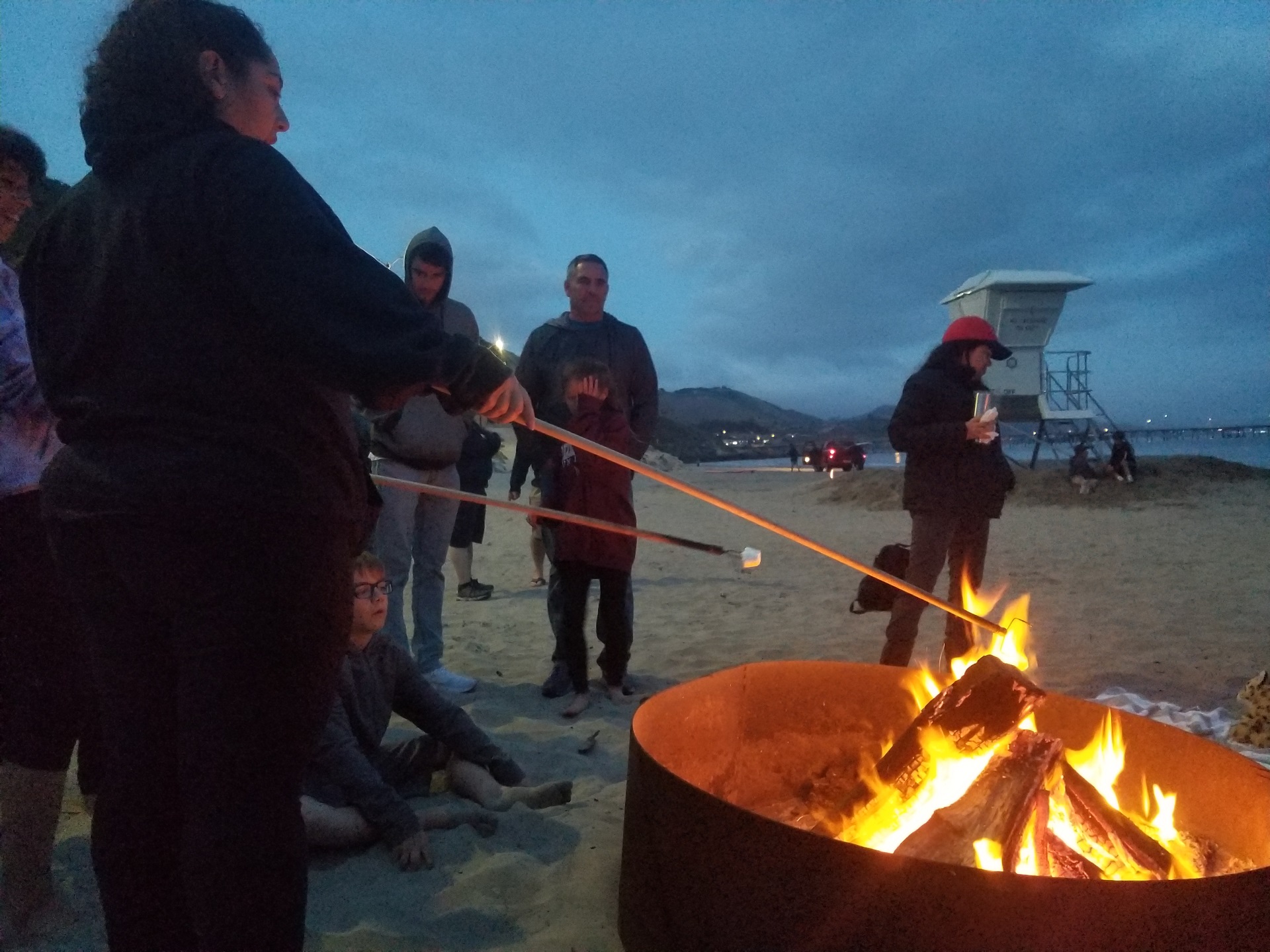 group of people roasting marshmallows at camp fire at night